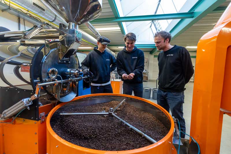 Los hermanos detrás de Café du Jour junto al tostador en su propio tostadero